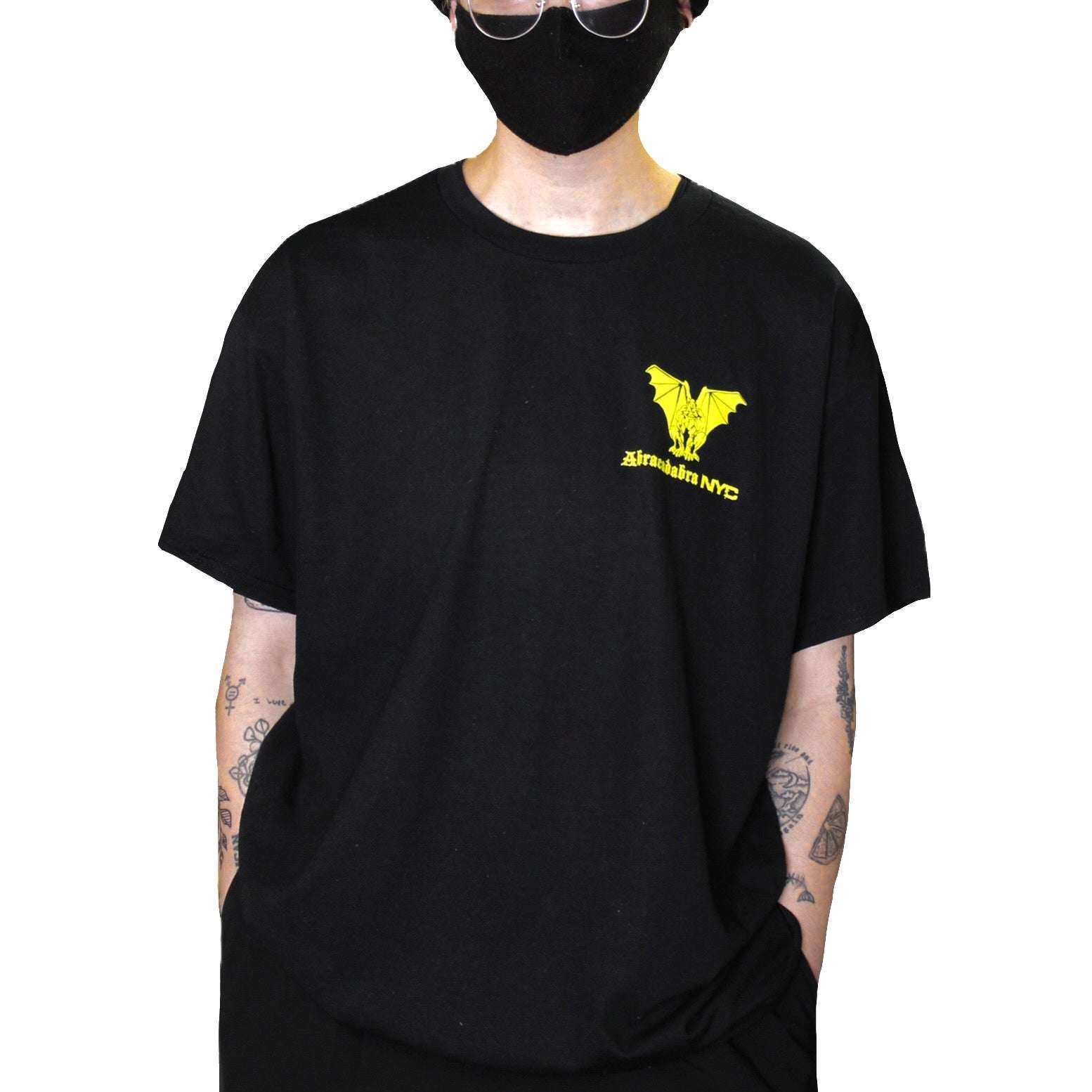 Model wearing a black Abracadabra NYC T-shirt with a yellow gargoyle logo on the chest.